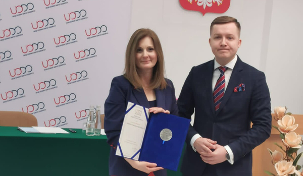 A woman in a jacket receiving an award from a man in a suit
