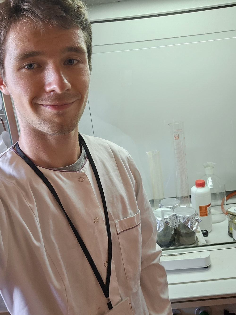 Kolorowe zdjęcie przedstawiające Jarosława Brodeckiego podczas badań. Student znajduje się w laboratorium i ubrnay jest w biały fartuch ochronny